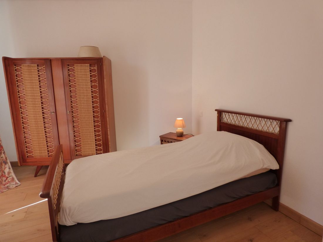 Chambre avec lit simple en bois et armoire en rotin