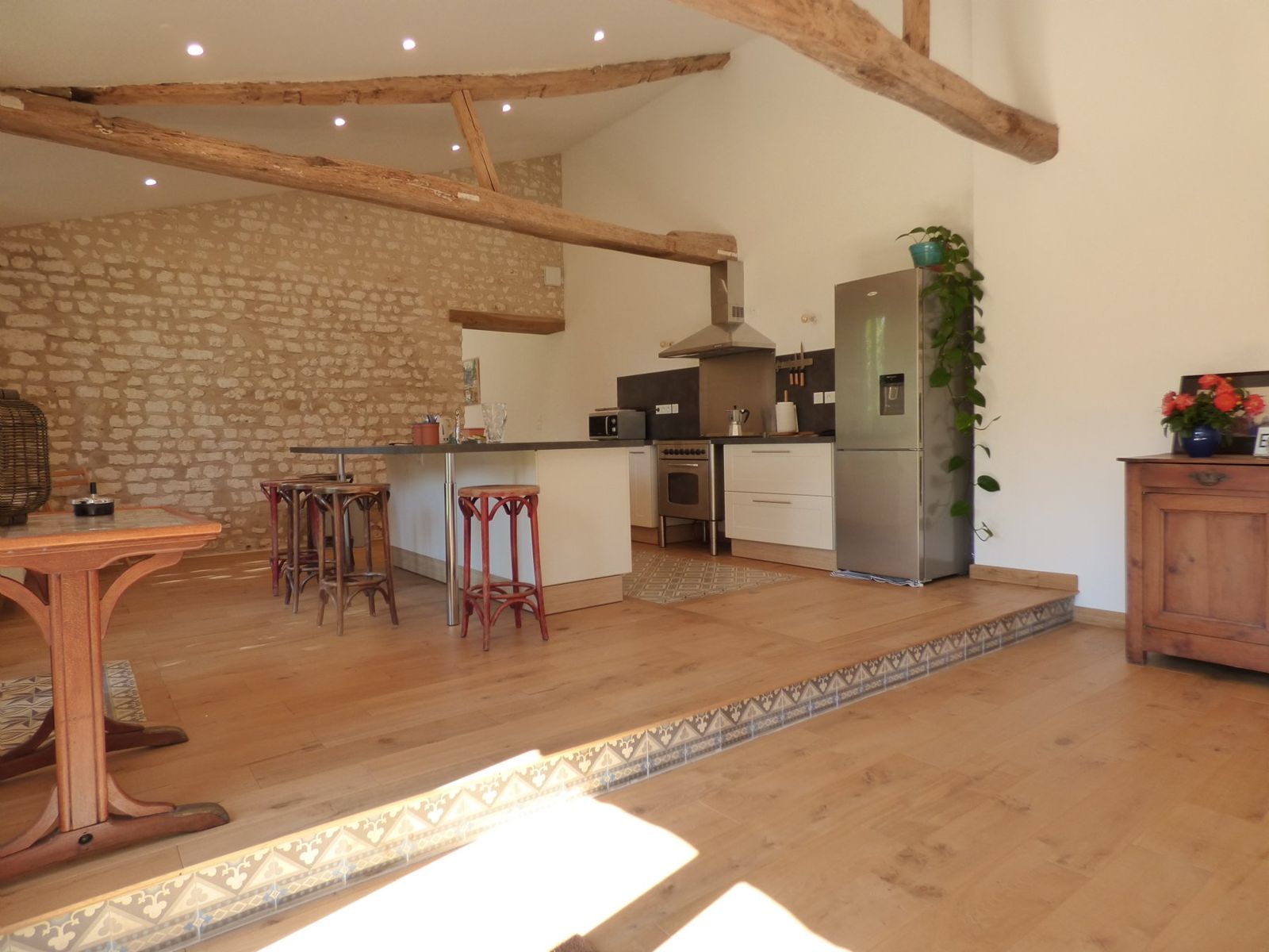 Grande pièce de vie sous les poutres, avec cuisine ouverte et mur en pierre